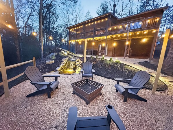 Eine Holzhütte mit Terrasse, Sitzgelegenheiten im Freien und einem kleinen Teich.
