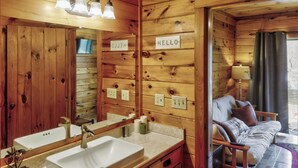 Interior de una cabaña de madera con baño, una cama y un letrero que dice 'HELLO'.