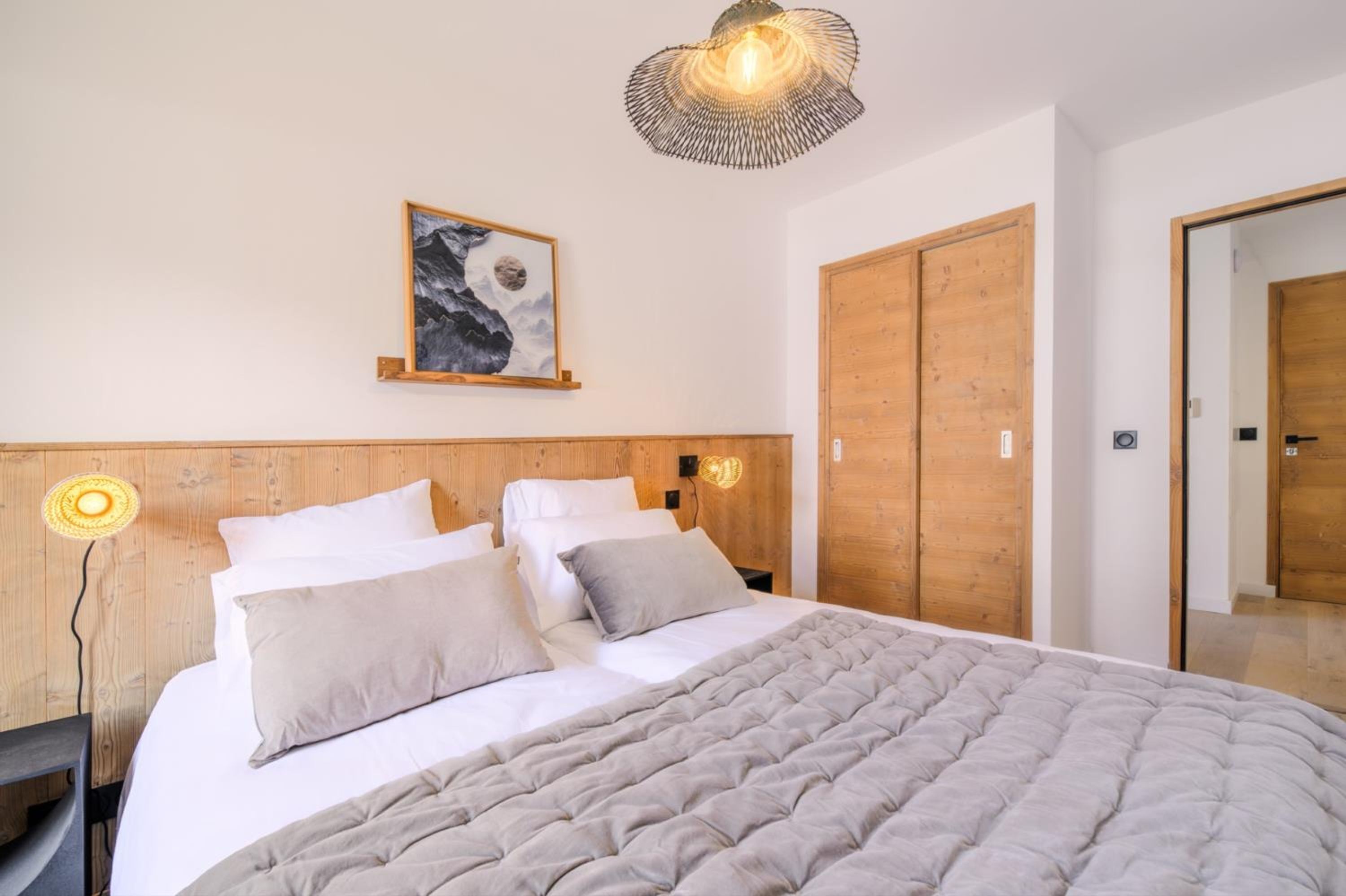 A bedroom with a wooden headboard, a bed with white bedding, a wall-mounted picture, and a pendant light.