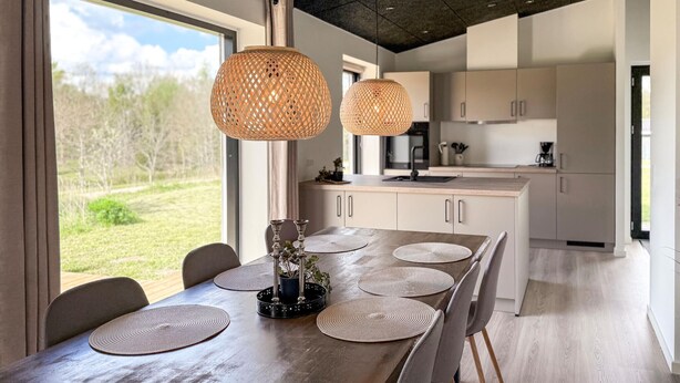Una cocina moderna con comedor, ventanas amplias y dos lámparas colgantes.