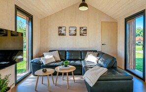 A modern living room with a black leather sectional sofa, wooden flooring, and large windows offering a view of the outdoors. - Lovely home in Sunds with WiFi (Sunds)