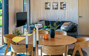 A modern living room with a wooden dining table, chairs, a flat-screen TV, a sofa, and a large window. - Lovely home in Sunds with WiFi (Sunds)