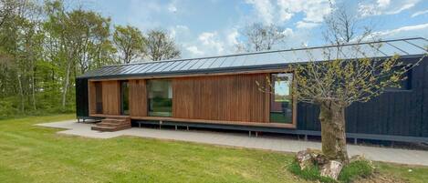 Een modern huis met een houten gevel, grote ramen en een boom in de voortuin.