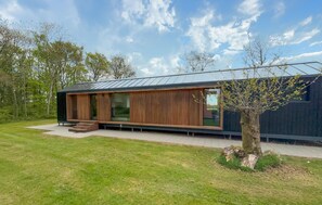 A modern house with a wooden exterior, large windows, and a tree in the yard.