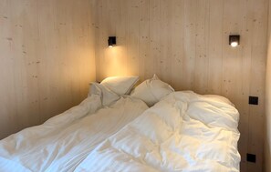 Una cama con ropa de cama blanca en una habitación con paredes de madera y dos luces fijadas a la pared.
