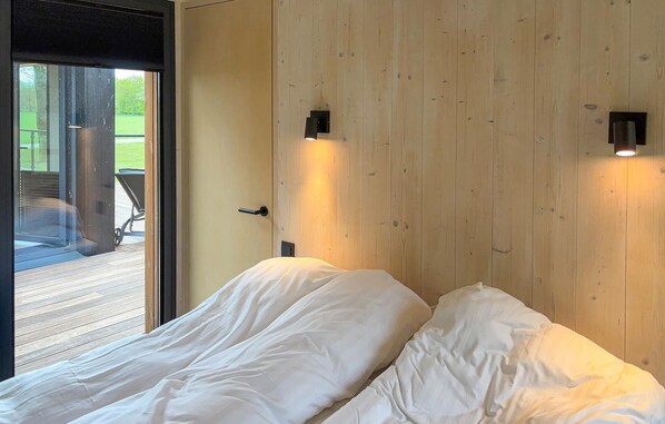 Un dormitorio con pared de madera, una puerta corredera de vidrio que da a un área exterior y dos lámparas de noche.