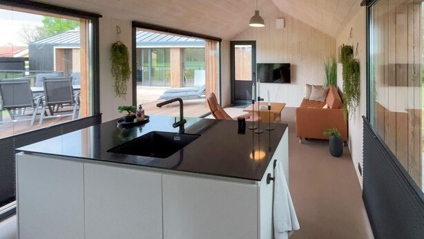A modern kitchen with a central island, a dining area with a sofa and chairs, and a TV mounted on the wall. - Lovely home in Sunds with WiFi (Sunds)