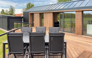 A modern outdoor deck with a table and chairs, large sliding glass doors, and a metal roof.