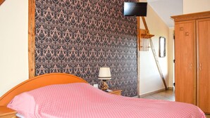 Une chambre à coucher avec un lit, une table de chevet, une lampe, une armoire et un téléviseur fixé au mur.