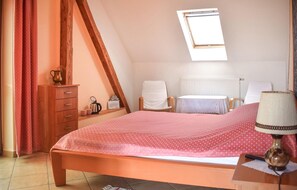 Un dormitorio con techo inclinado, una cama con colcha rosa, un aparador de madera, un radiador y una mesita de noche con lámpara.