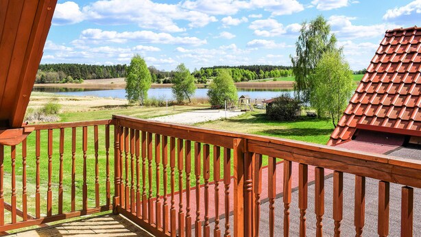 Une terrasse en bois offrant une vue sur un lac, des arbres et un bâtiment au toit rouge.