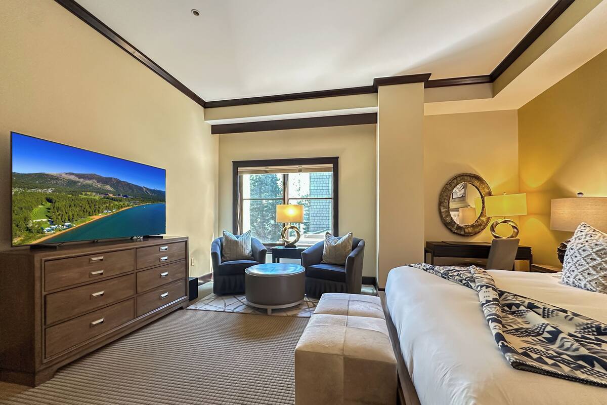 A hotel room with a large flat-screen TV, a bed, a sofa, a coffee table, a desk, and a window.