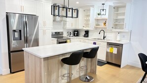 Eine moderne Küche mit weißen Schränken, Edelstahlgeräten, einer zentralen Kochinsel mit Barhocker und Pendelleuchten.