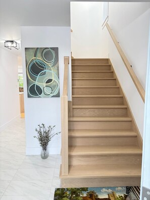 Un escalier avec des marches en bois et une rampe, un tableau abstrait accroché au mur, et une petite plante en pot.