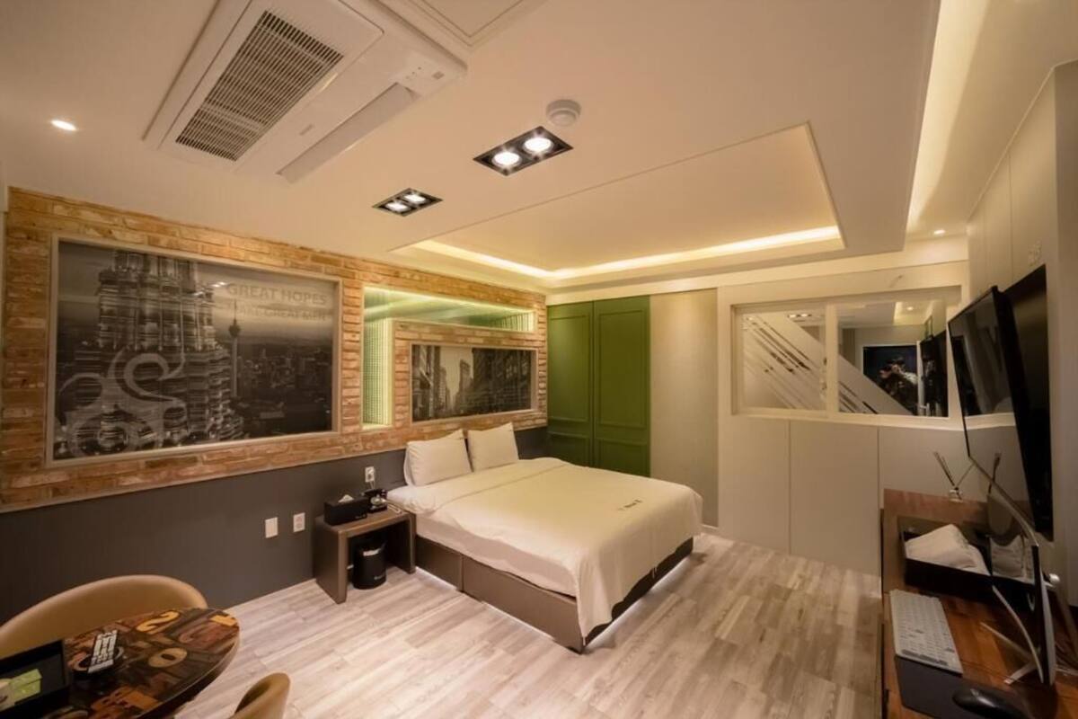 A modern hotel room with a bed, a desk, a chair, a TV, and a large mirror.