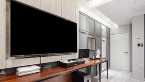A modern bathroom with a large mirror, a flat-screen TV, and a wooden vanity.