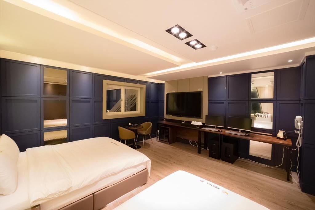 A hotel room with a bed, desk, TV, and a mirror.