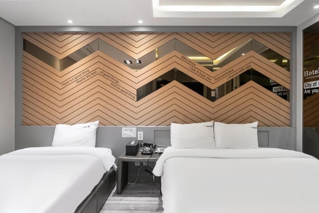 Une chambre d’hôtel avec deux lits, un bureau, un téléphone et un mur orné de citations inspirantes.