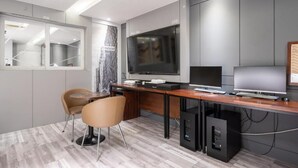 A modern room with a large flat-screen TV, a wooden desk, two chairs, and built-in cabinets.