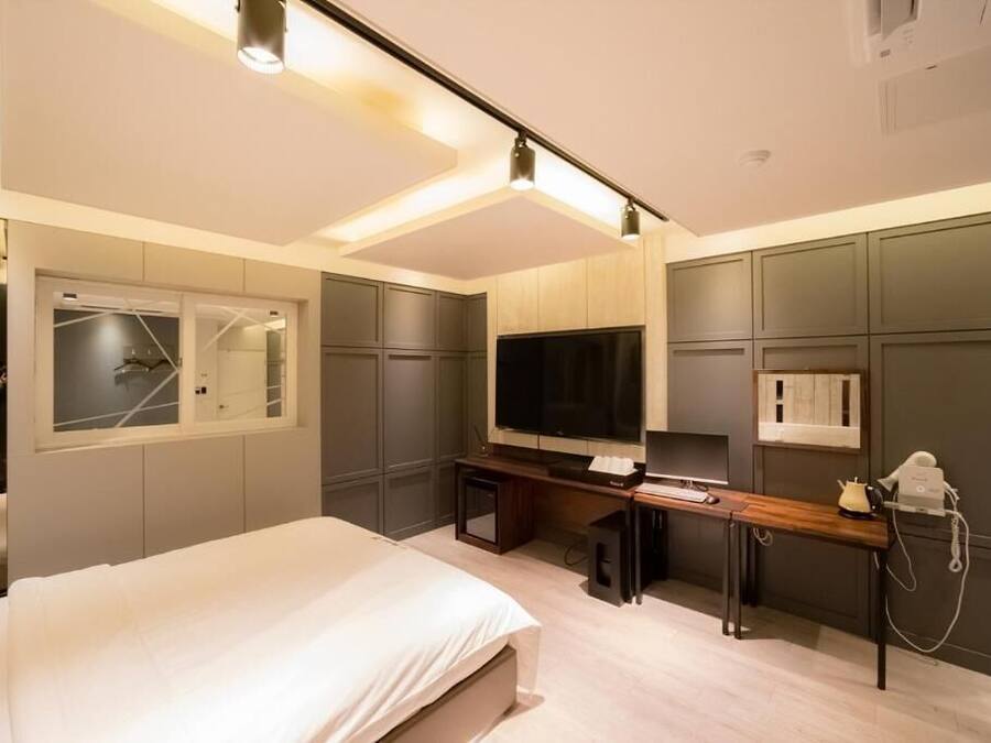 A modern hotel room with a bed, a desk, a television, and a minibar.