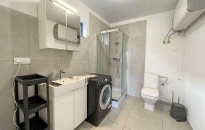 Une salle de bain moderne équipée d’un lave-linge, de toilettes, d’une douche et d’un lavabo.
