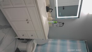 Casa de banho com toucador branco, espelho e sanita.
