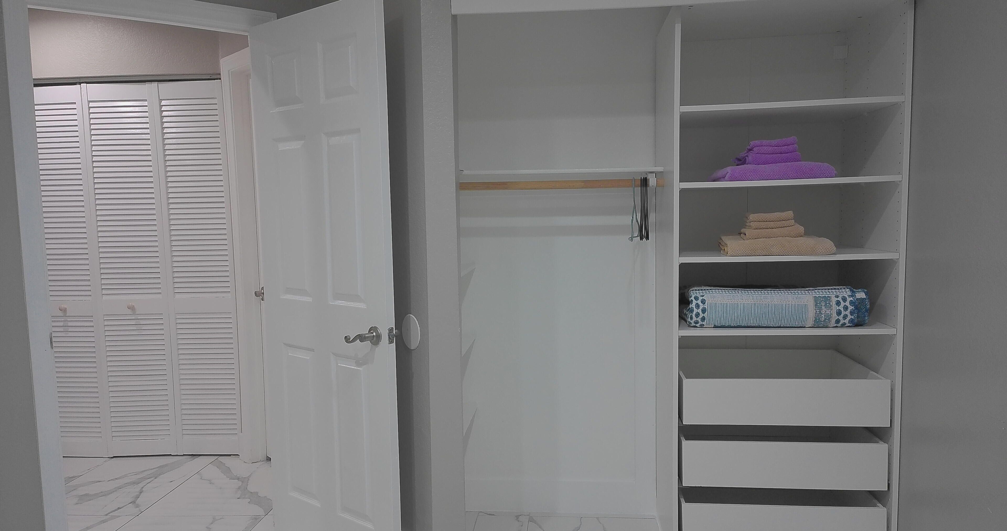 Un armario blanco con varios estantes, una puerta cerrada con paneles persiana y un suelo de mármol.