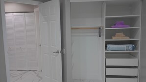 Um guarda-roupa branco com várias prateleiras, uma porta fechada com painéis venezianos e piso de mármore.