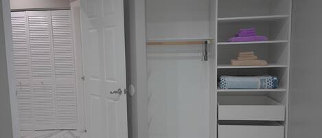 A white wardrobe with multiple shelves, a closed door with louvered panels, and a marble floor.