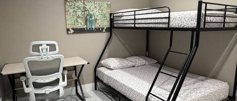 Ein Stockbett mit Schreibtisch und Stuhl, ein Bild an der Wand und ein Fliesenboden.