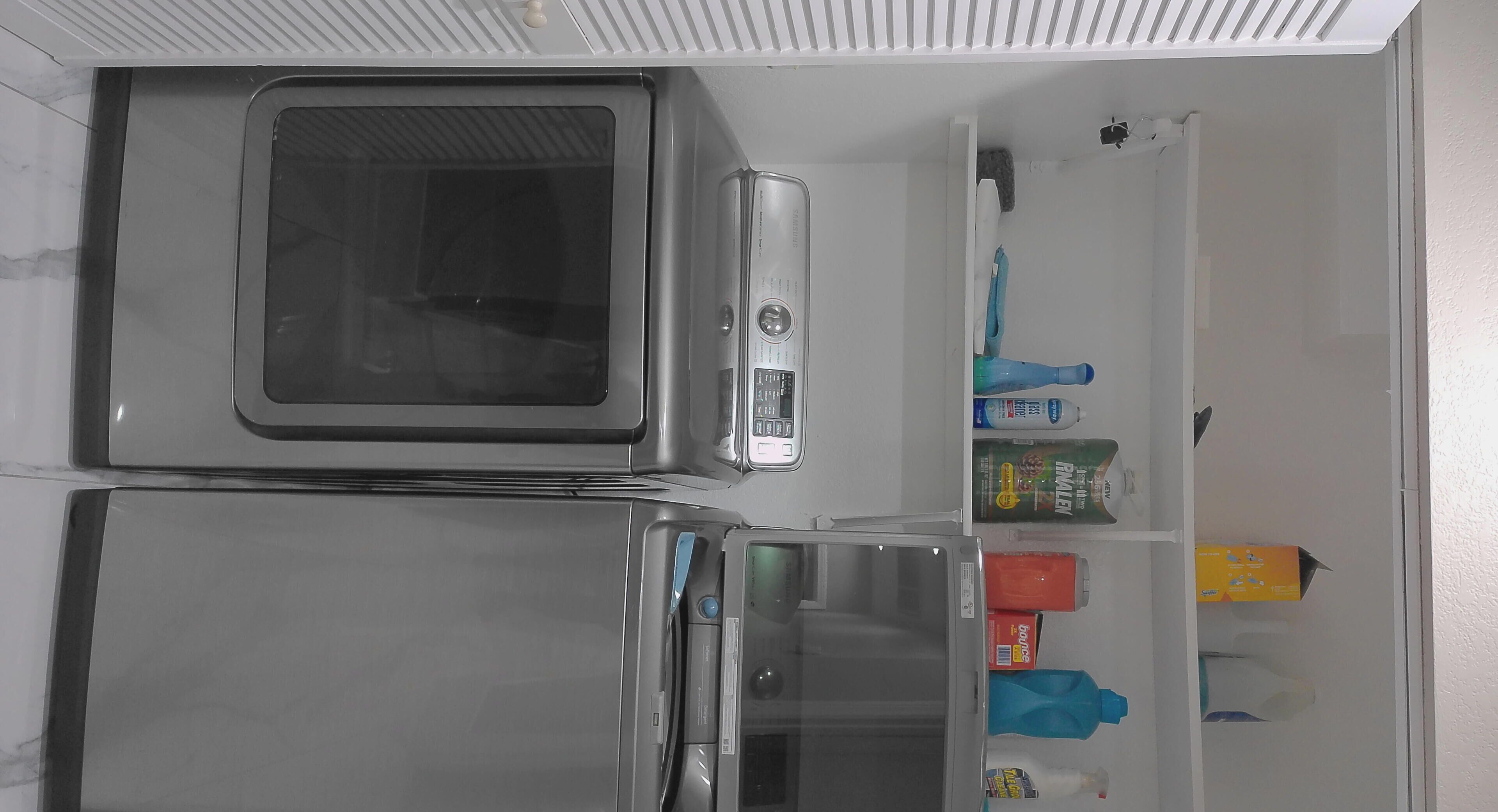 Una cocina con microondas, refrigerador y una estantería con diversos objetos, incluyendo una botella y una caja.