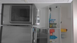 Cozinha equipada com micro-ondas, frigorífico e prateleira com diversos objetos, incluindo uma garrafa e uma caixa.