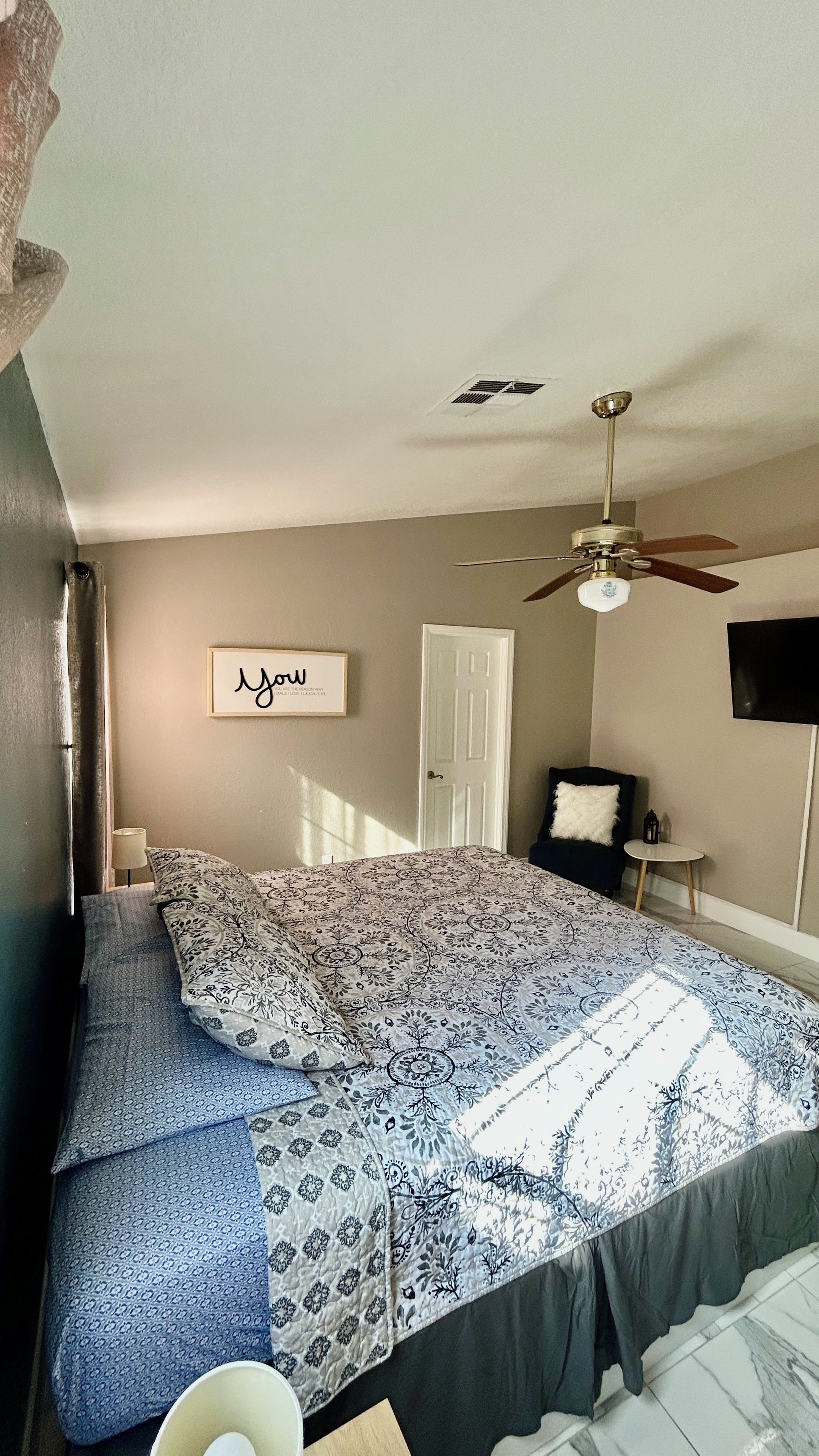 A bedroom with a bed, a ceiling fan, a door, and a wall-mounted TV.