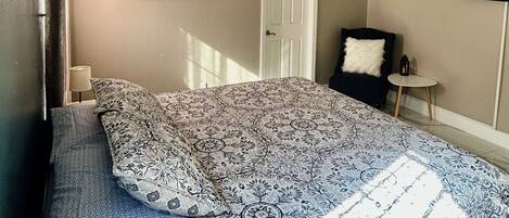 A bedroom with a bed, a ceiling fan, a door, and a wall-mounted TV.