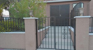 Una entrada portonada con un portón metálico, un sendero de concreto y un edificio con una pared texturizada y una puerta grande.