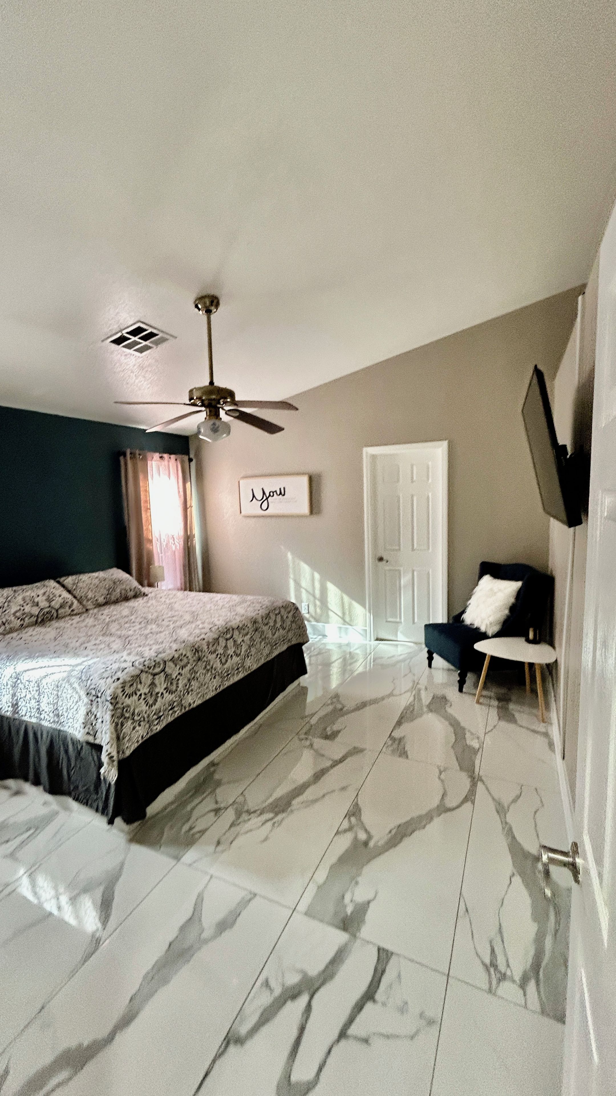 A bedroom with a bed, a ceiling fan, a door, and a wall-mounted TV.