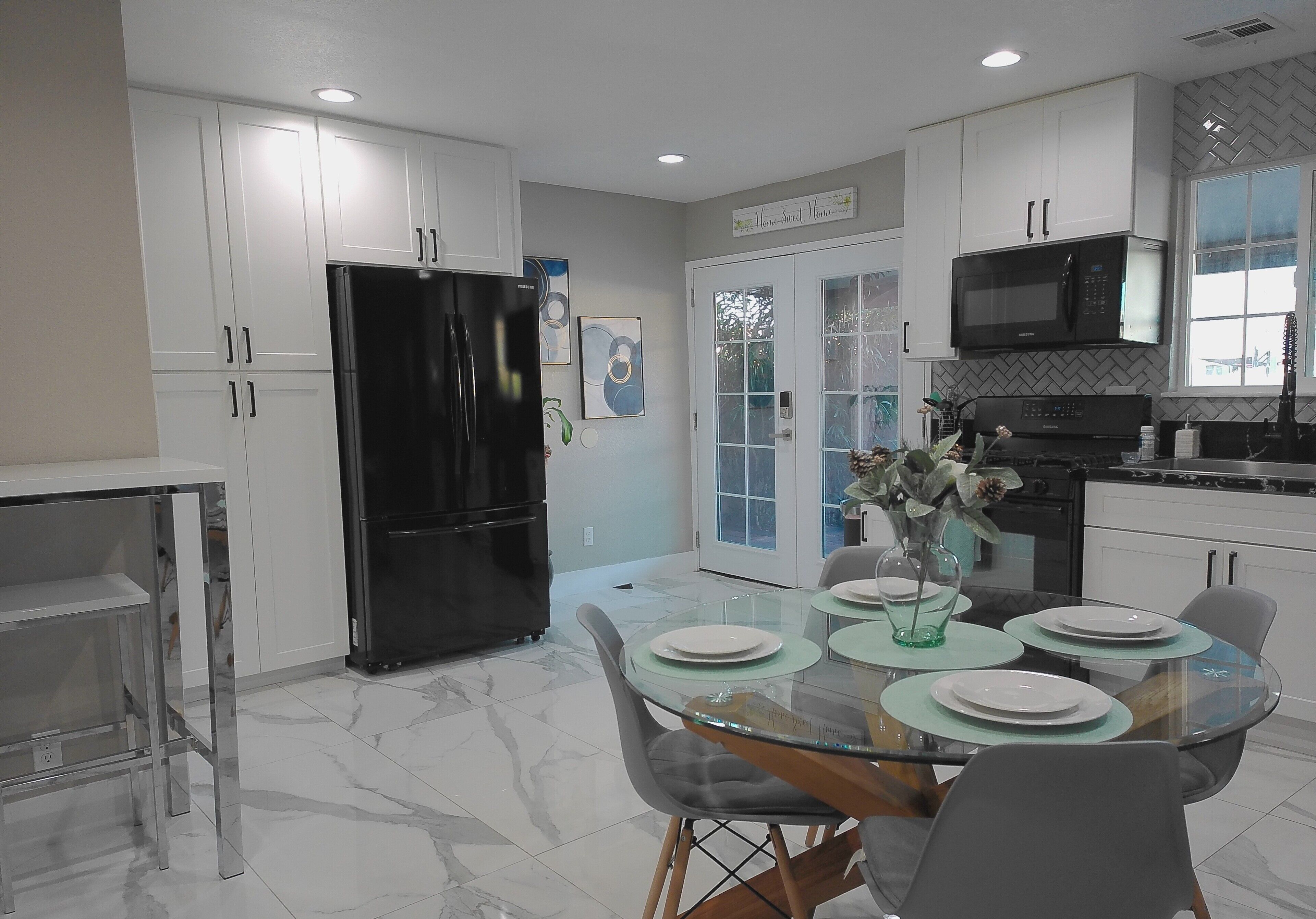 A modern kitchen with white cabinets, a black refrigerator, a microwave, and a dining area with a glass table and chairs.