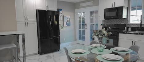 A modern kitchen with white cabinets, a black refrigerator, a microwave, and a dining area with a glass table and chairs.