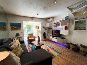 Ein modernes Wohnzimmer mit Sofa, Couchtisch, Fernseher und Küchenzeile inklusive Schränken und Esstisch.