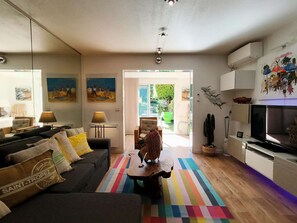 Ein modernes Wohnzimmer mit einer Couch, einem Couchtisch und einem Fernseher. Auf dem Boden liegt ein farbenfroher Streifen Teppich.
