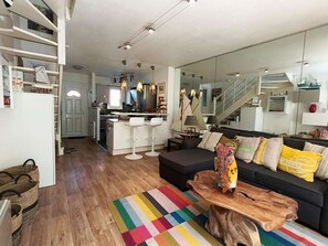 Ein modernes Wohnzimmer mit einer Couch, einem bunten Teppich, einem Holztisch und einer Küche im Hintergrund.