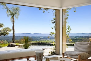 A room with a large window, a sofa, a chair, and a view of a landscape with hills and a body of water. - Air-conditioned dream villa with lagoon-style pool and sea view for 6 guests in La Londe-les-Maures (LA LONDE LES MAURES)