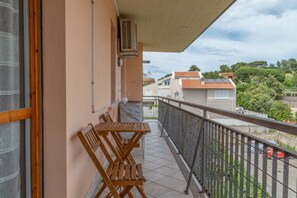 Ein Balkon mit Tisch und Stühlen, ein Fenster und Blick auf benachbarte Gebäude und Grünflächen.
