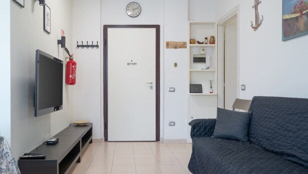 A room with a TV, a door, a shelf with items, and a bed. - APPARTAMENTO SOTTOBOMBA (Portoferraio)