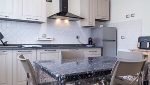 A modern kitchen with white cabinets, a black range hood, a refrigerator, and a dining table with chairs. - APPARTAMENTO SOTTOBOMBA (Portoferraio)