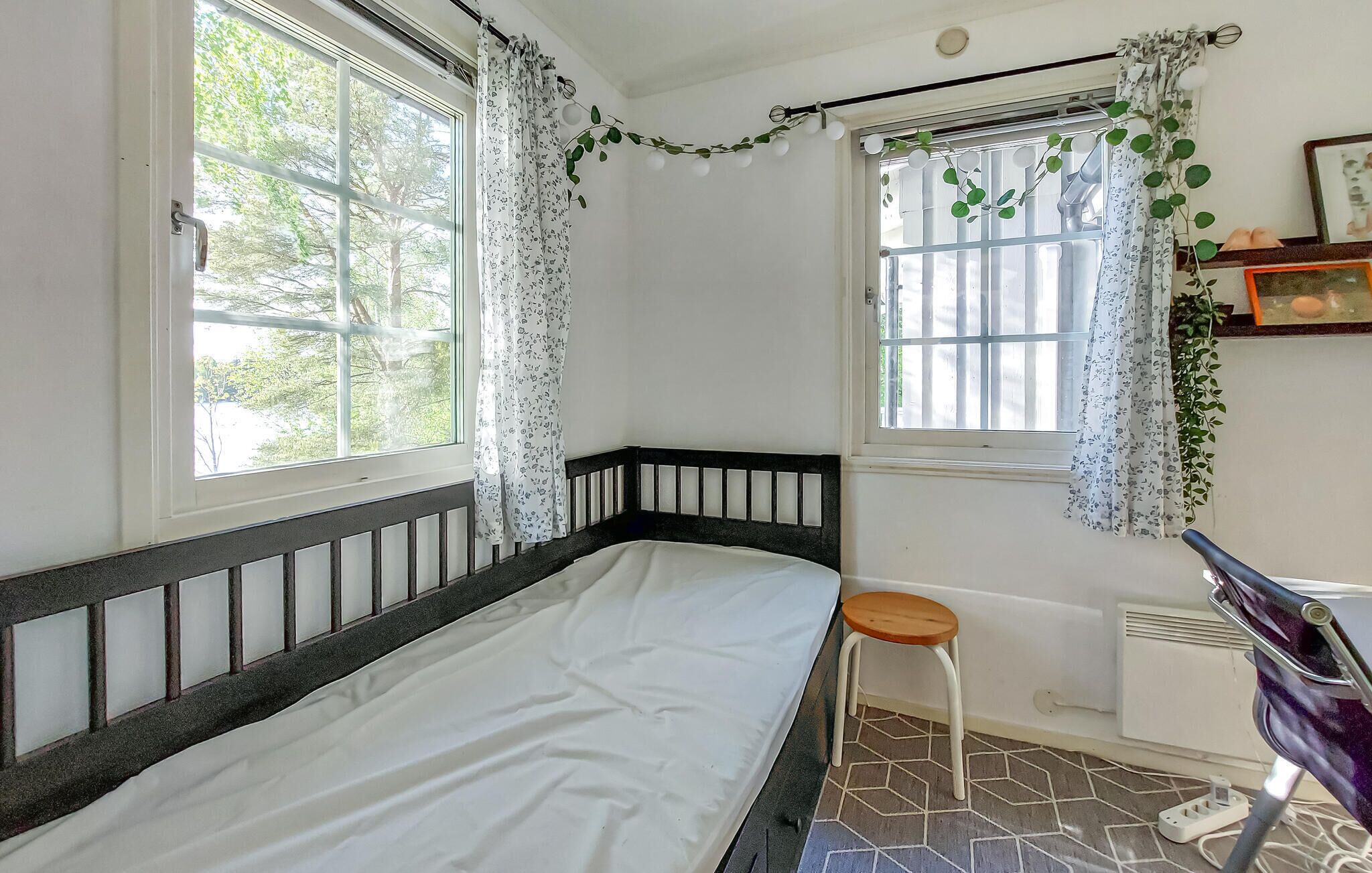 A room with a bed, a window with curtains, a radiator, and a chair.