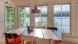 En matplats med ett bord och stolar, stora fönster med utsikt över en sjö och en hänglampa.