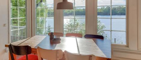 Ein Essbereich mit Tisch und Stühlen, große Fenster mit Seeblick und einer Pendelleuchte.