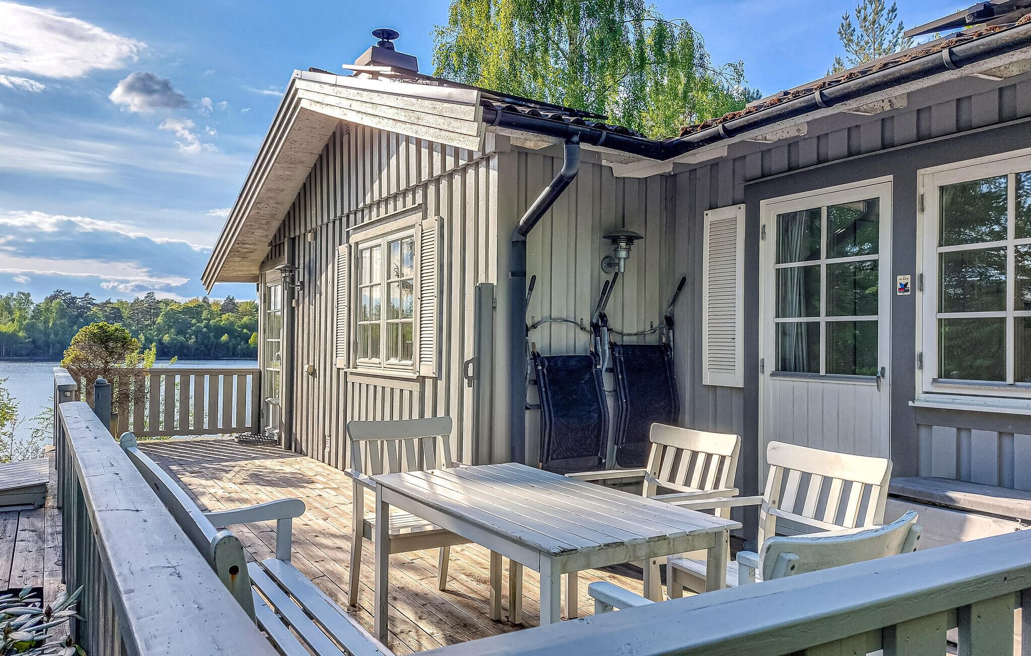 A wooden cabin with a deck, outdoor seating, and a view of a lake.