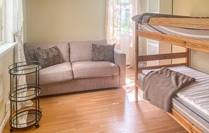 A bunk bed with a mattress, a sofa with floral cushions, and a metal side table with a patterned cloth. - 1 bedroom nice home in Växjö (Växjö)